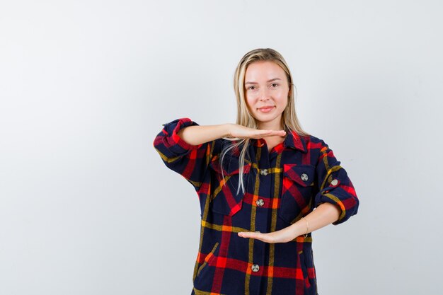 Señorita mostrando signo de tamaño en camisa a cuadros y mirando confiado, vista frontal.