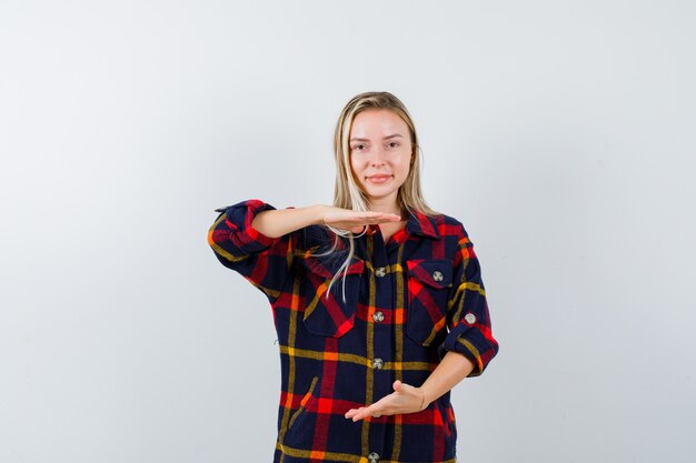 Señorita mostrando signo de tamaño en camisa a cuadros y mirando confiado, vista frontal.