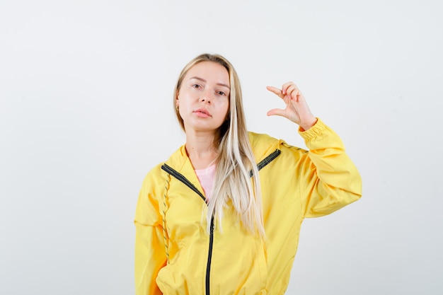 Señorita mostrando signo de tamaño pequeño en camiseta, chaqueta y mirando confiado