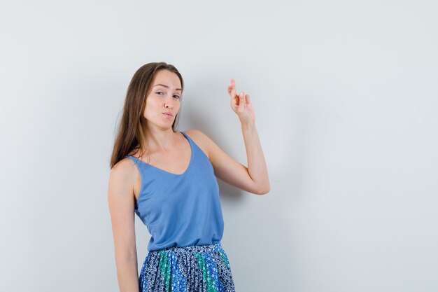 Señorita mostrando sus dedos cruzados en blusa azul, falda y mirando confiado, vista frontal.