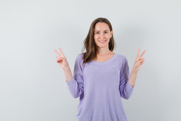 Señorita mostrando V-sign en camisa casual y mirando alegre