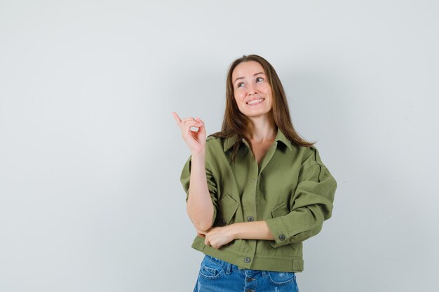 Señorita en pantalones cortos de chaqueta apuntando a la esquina superior izquierda y mirando esperanzada