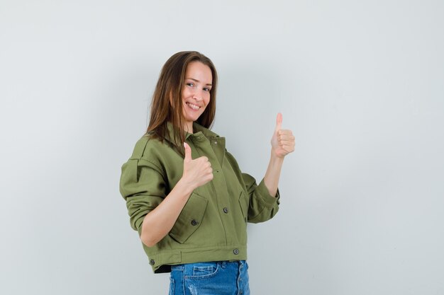 Señorita en pantalones cortos de chaqueta verde mostrando doble pulgar hacia arriba y mirando dichoso