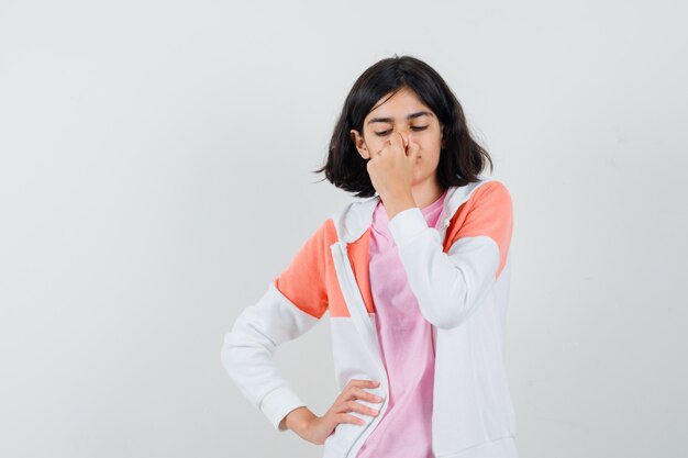 Señorita pellizcando su nariz en chaqueta, camisa rosa y mirando en silencio