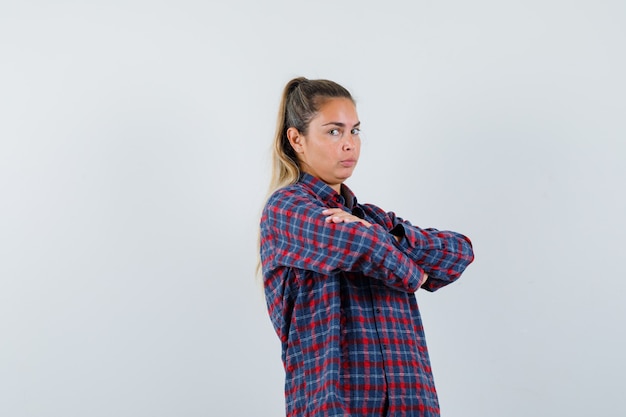 Foto gratuita señorita de pie con los brazos cruzados en camisa a cuadros y mirando confiado, vista frontal.