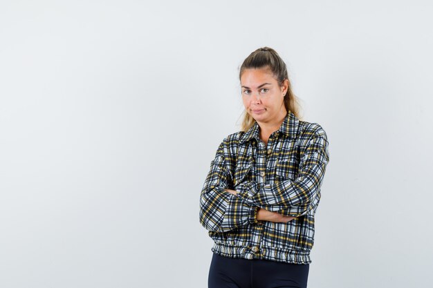 Señorita de pie con los brazos cruzados en camisa, pantalones cortos y mirando confiada. vista frontal.