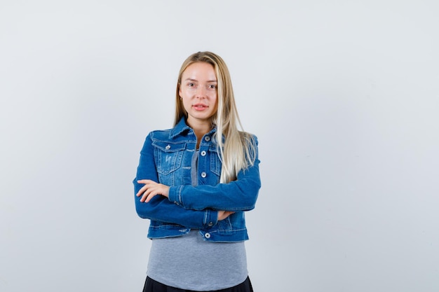 Señorita de pie con los brazos cruzados en camiseta, chaqueta vaquera, falda y luciendo confiada.