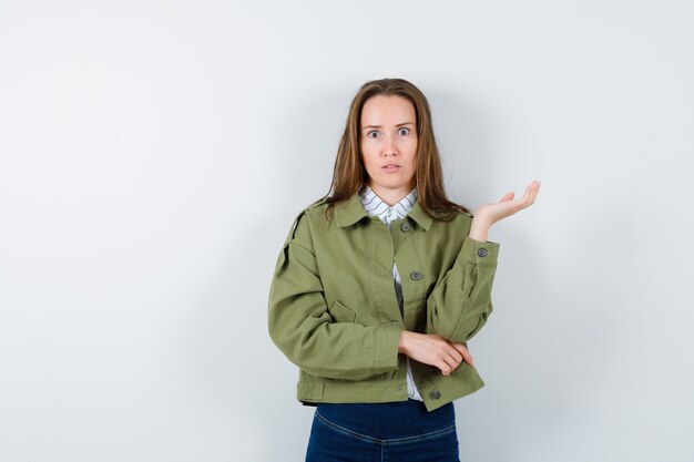 Señorita de pie con la palma extendida en blusa, chaqueta y mirando desconcertado.