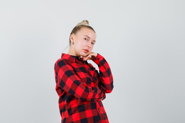 Señorita de pie en pose de pensamiento en camisa a cuadros y mirando bastante