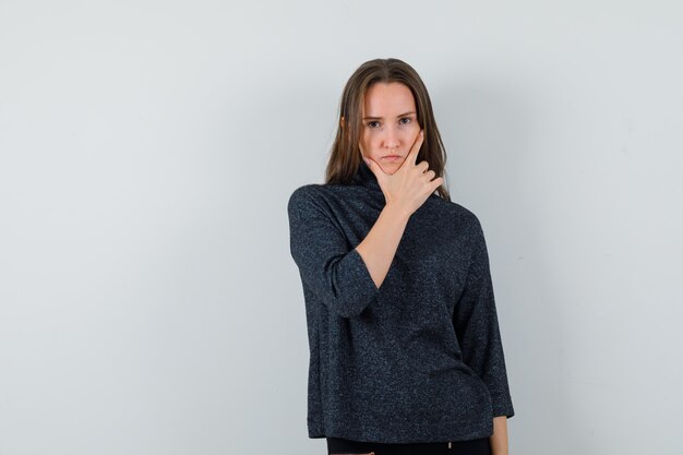 Señorita de pie en pose de pensamiento en camisa y mirando sensible