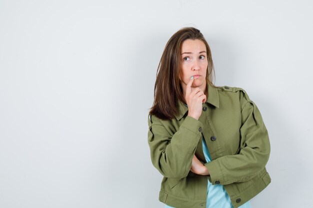 Señorita de pie en pose de pensamiento en camiseta, chaqueta y mirando pensativo, vista frontal.