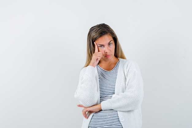 Señorita de pie en pose de pensamiento en camiseta, chaqueta y mirando triste, vista frontal.