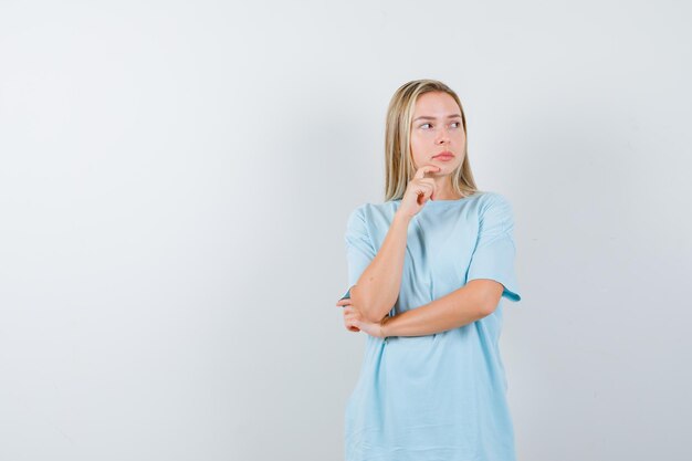 Señorita de pie en pose de pensamiento en camiseta y mirando indeciso aislado