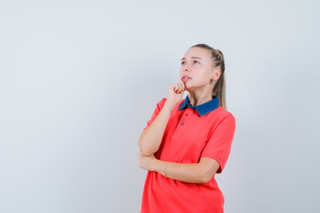 Señorita de pie en pose de pensamiento en camiseta y mirando preocupado