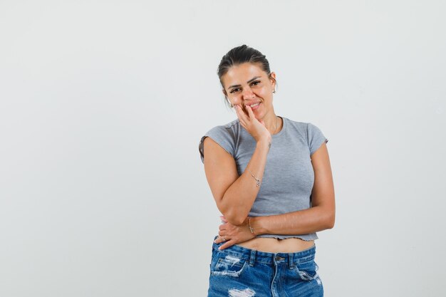 Señorita de pie en pose de pensamiento en camiseta, pantalones cortos y aspecto alegre.