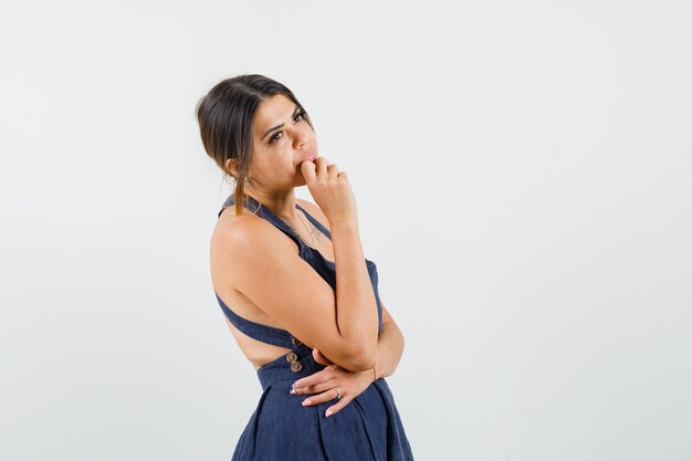 Señorita de pie en pose de pensamiento vestido y mirando soñadora.