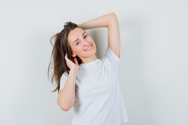 Señorita posando con la mano en la cabeza en camiseta blanca y mirando seductor