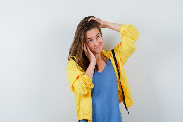 Señorita posando con la mano en la cabeza en camiseta, chaqueta y mirando vacilante