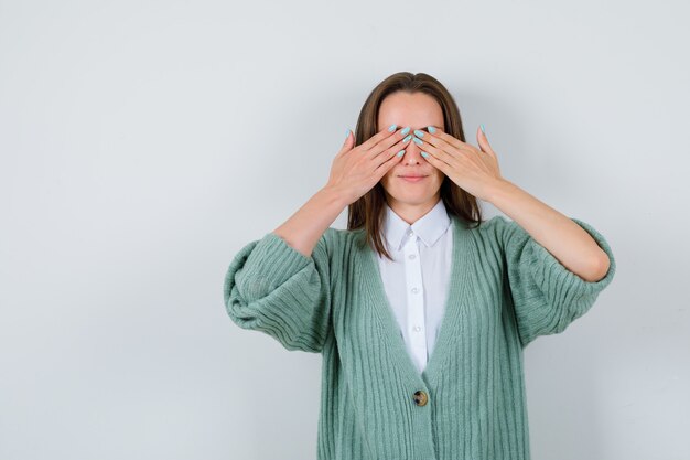 Señorita que cubre los ojos con las manos en camisa, chaqueta y parece complacida. vista frontal.