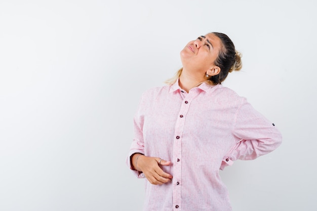 Foto gratuita señorita que sufre de dolor de espalda en camisa rosa y con aspecto cansado