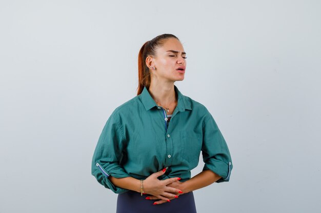 Señorita que sufre de dolor de estómago en camisa verde y luce dolorosa. vista frontal.