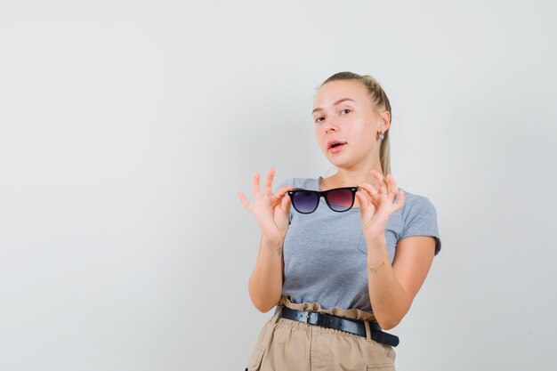 Señorita quitándose las gafas en camiseta y pantalón y mirando confiado