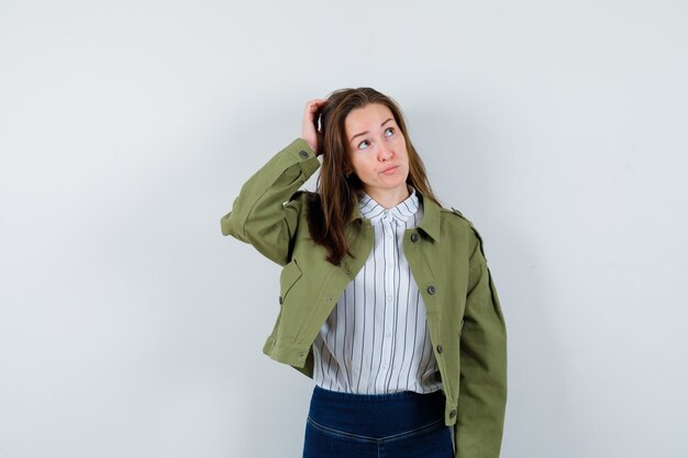 Señorita rascándose la cabeza en camisa, chaqueta y mirando pensativo, vista frontal.