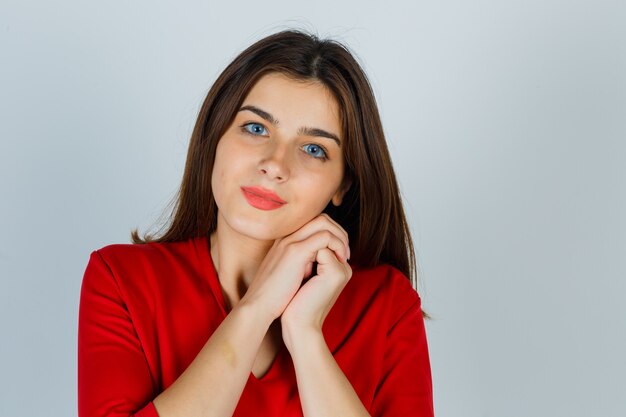 Señorita recostada mejilla en sus manos en blusa roja y luciendo hermosa