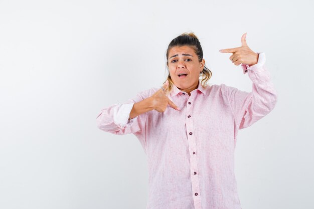 Señorita señalando a sí misma en camisa rosa y mirando ansiosa