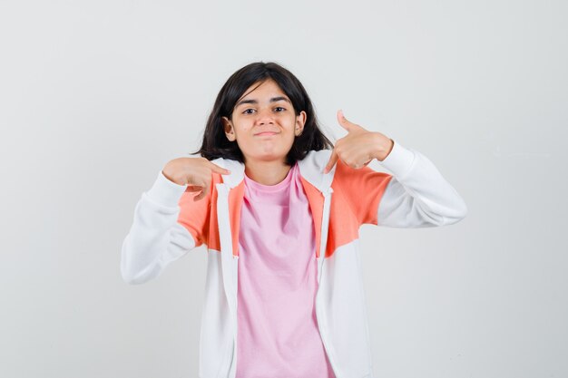 Señorita señalando a sí misma en chaqueta, camisa rosa y mirando confiada.