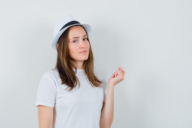 Señorita con sombrero de camiseta blanca mirando a la cámara mientras piensa y parece sensato