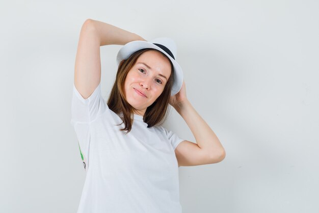 Señorita con sombrero de camiseta blanca tomados de la mano en la cabeza y mirando confiado