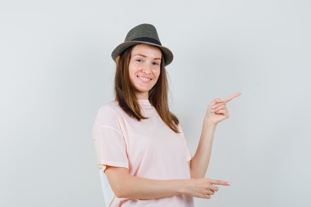 Señorita con sombrero de camiseta rosa apuntando hacia el lado derecho y mirando alegre