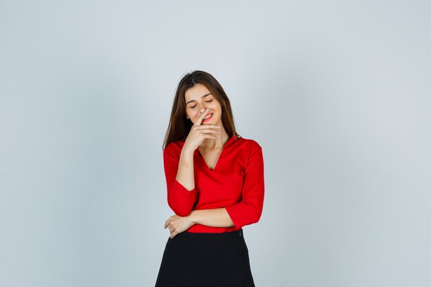 Señorita sonriendo mientras posa en blusa roja, falda y mirando alegre