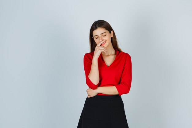 Señorita sonriendo mientras posa en blusa roja, falda y mirando alegre