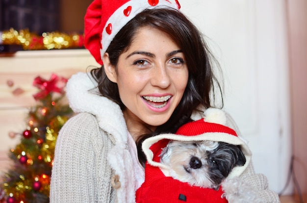 Señorita sonriente con su perro llevando el disfraz de santa