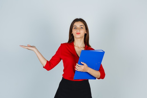 Señorita sosteniendo la carpeta mientras muestra algo en blusa roja