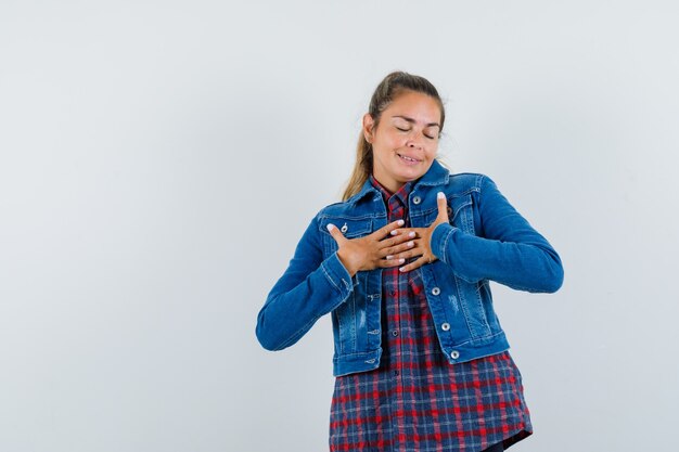 Señorita sosteniendo los dedos apretados en el pecho en camisa, chaqueta y mirando feliz. vista frontal.