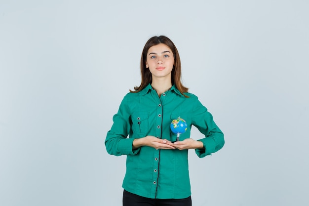 Señorita sosteniendo globo terráqueo en camisa y mirando complacido. vista frontal.