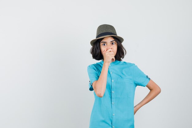 Señorita sosteniendo la mano en la boca con camisa azul, sombrero y mirando preocupado.