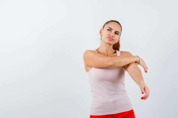 Señorita sosteniendo la mano en el brazo en camiseta sin mangas beige y mirando pensativo