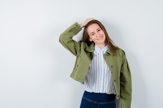 Señorita sosteniendo la mano en la cabeza en blusa, chaqueta y mirando encantador, vista frontal.