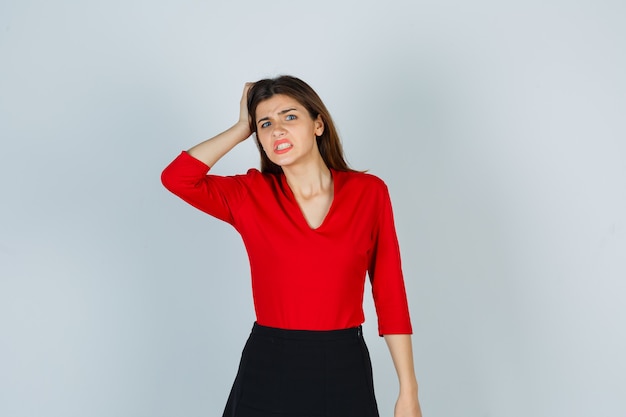 Foto gratuita señorita sosteniendo la mano en la cabeza en blusa roja, falda y mirando enojado