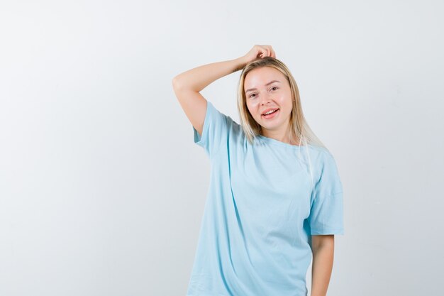 Señorita sosteniendo la mano en la cabeza en camiseta y mirando alegre. vista frontal.