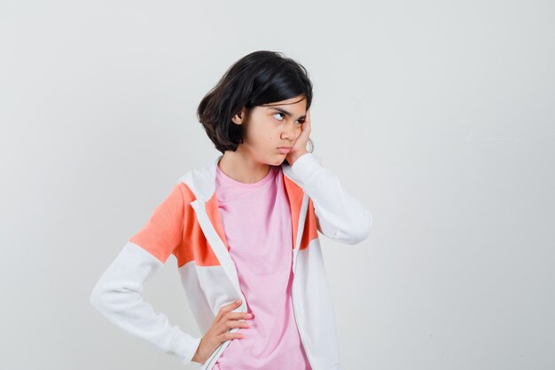 Señorita sosteniendo la mano en la cara mientras mira a un lado en chaqueta, camisa rosa y parece enojada.