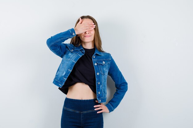 Señorita sosteniendo la mano en los ojos en blusa y mirando alegre, vista frontal.