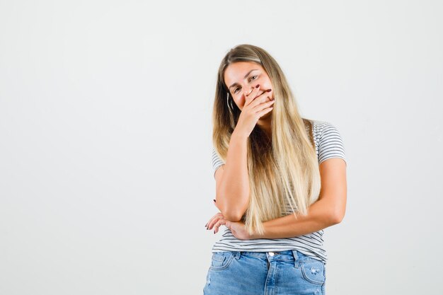 Señorita sosteniendo la mano en su boca mientras se ríe en camiseta y parece feliz. vista frontal.