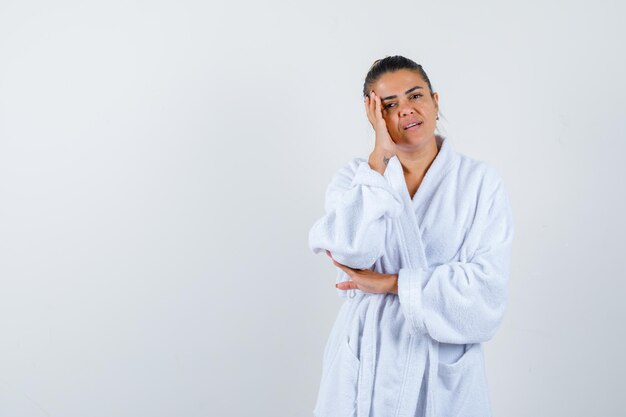 Señorita sosteniendo la mano en su sien en bata de baño y mirando confiada