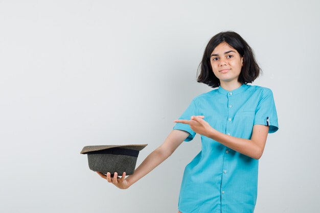 Señorita sosteniendo el sombrero hacia atrás mientras apunta con camisa azul