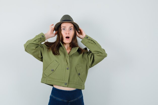 Señorita sosteniendo su sombrero en pantalones de chaqueta y mirando sorprendido